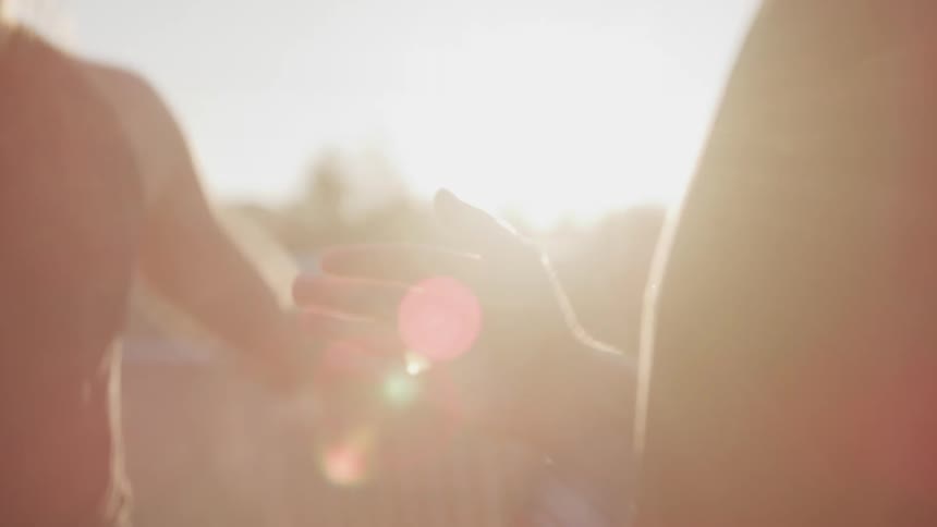 A woman jumps during a warmup as a man watches holding a stopwatch and clapping in the glow of sunset