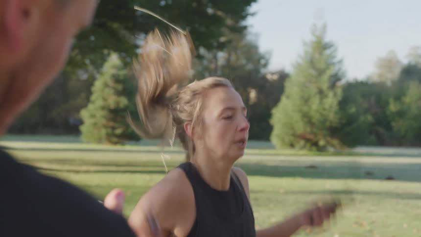 A young woman skipping rope in a public park at midday with a man standing beside her