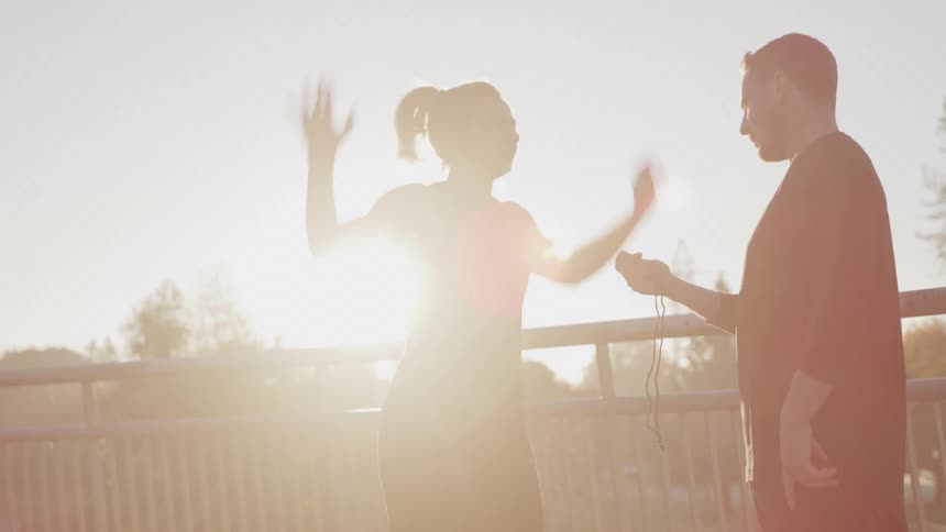 Female working out outdoors doing jumping jacks as her trainer times her