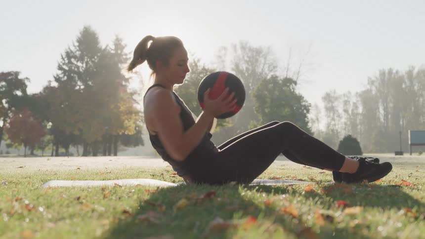 Woman performing an ab workout with a medicine ball on the grass at a park