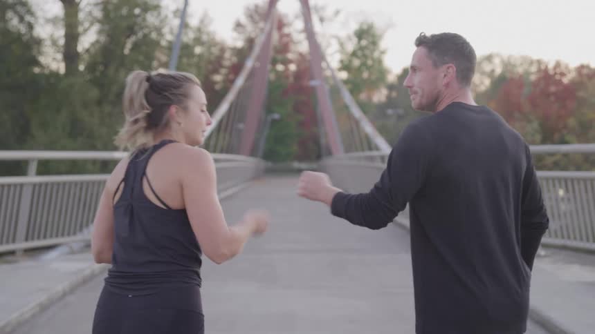 A white male and young female warm up and jog down the bridge in daytime