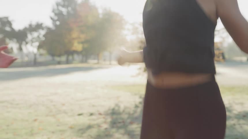 A woman skipping rope in the park at midday while a man beside her cheers her on