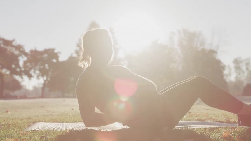 Woman doing an ab workout with medicine ball on grass against the sunlight