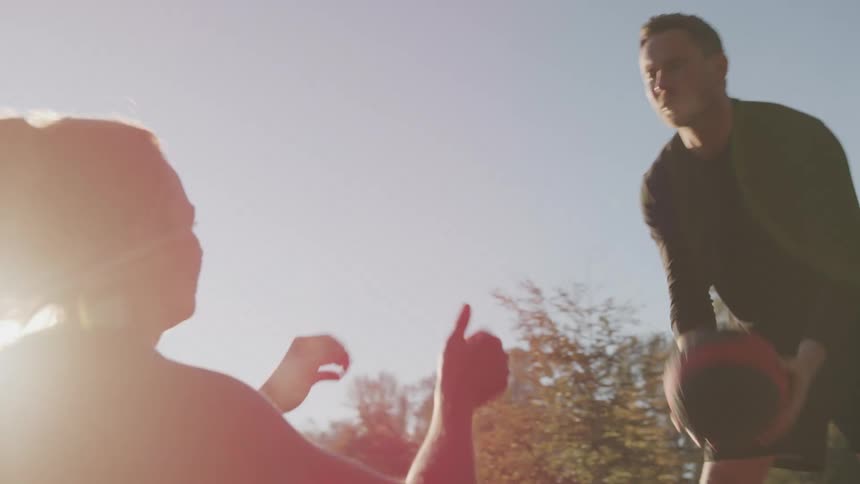 A woman throws a ball to a man while doing situps