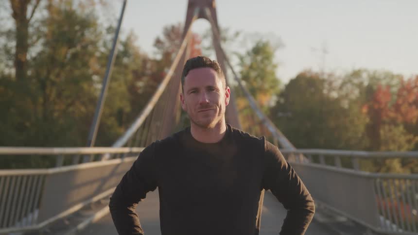 Portrait of a white male adult smiling while standing in the middle of a bridge in daytime