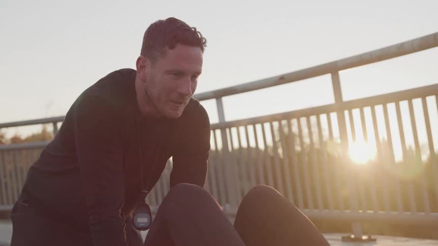 Male trainer helps a young white woman by holding her legs as she performs situps on a bridge during the day