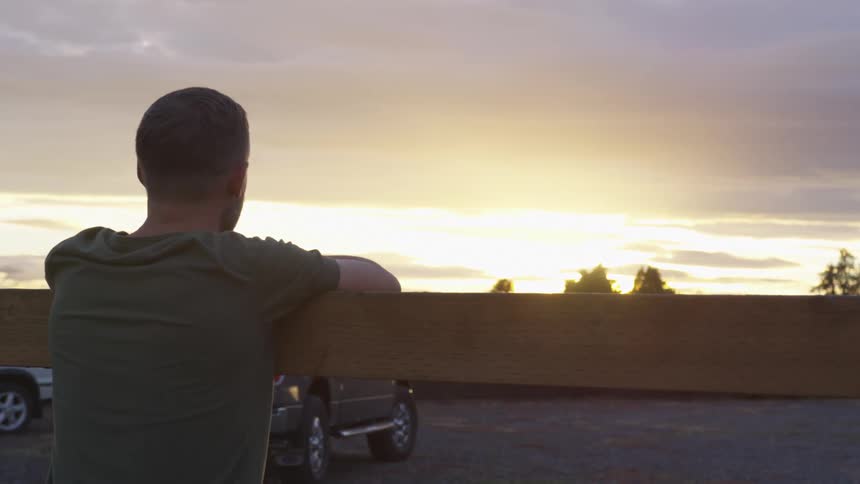A man leans on a wooden beam and watches the sunset