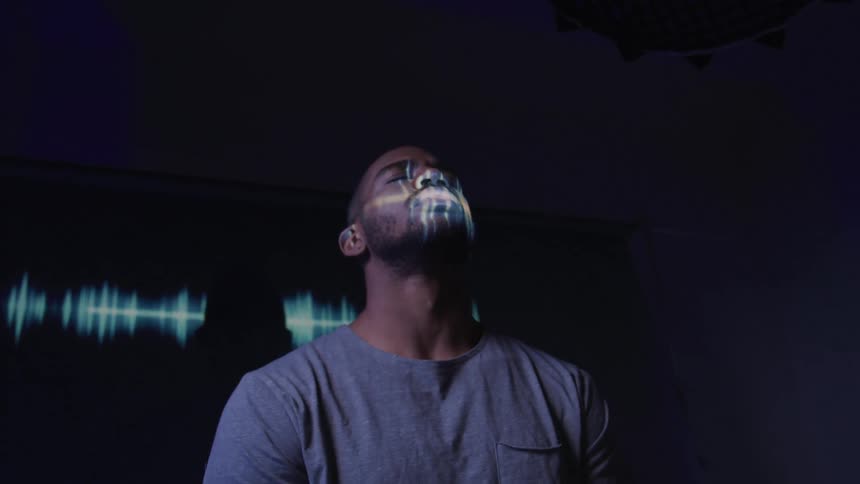 Lights form a pattern on a man and the wall behind him while he bends his head backward then forward