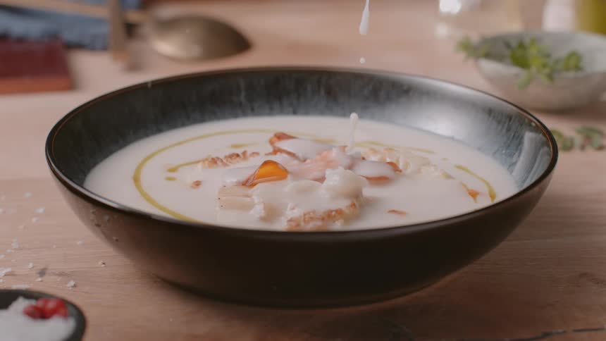 Creamy soup stirred in black bowl with oil and crispy toppings