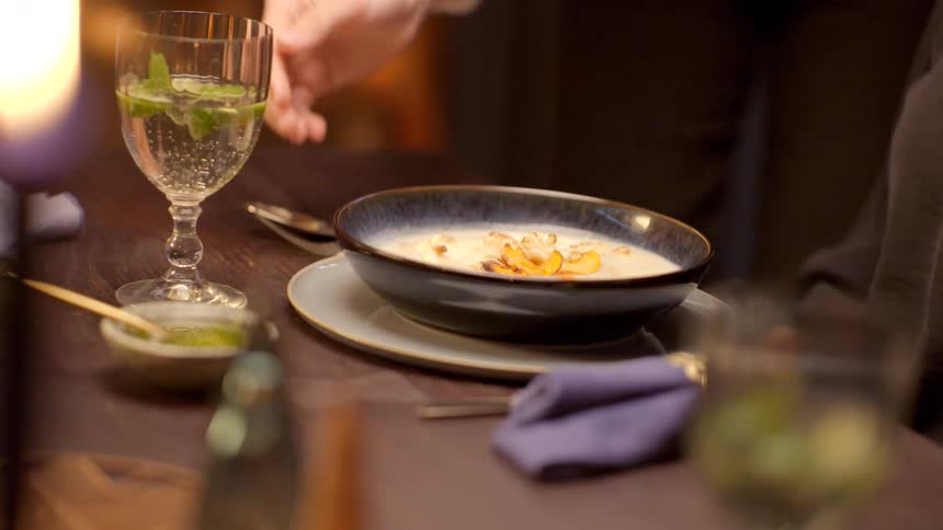 A waiter puts a bowl of soup on a charger plate in front of a diner