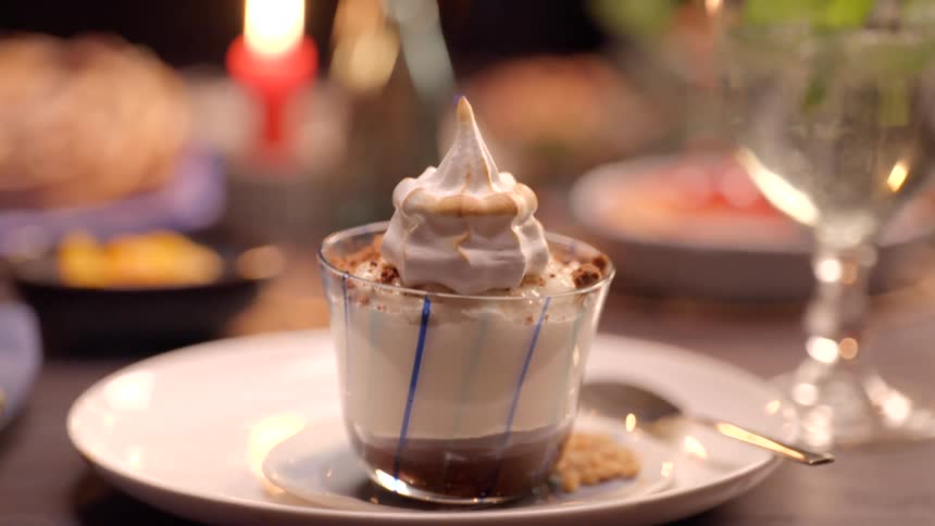 A creamy dessert with toasted meringue sits on a white plate in warm light