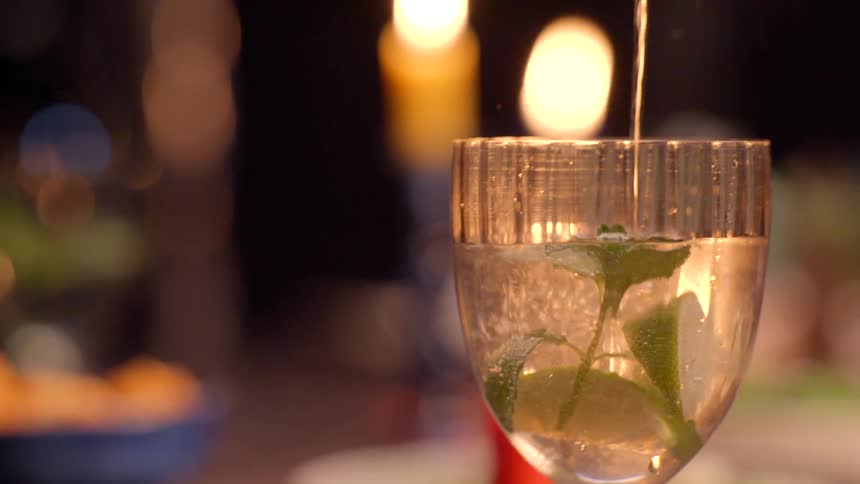 Alcohol being poured into a wine glass containing a slice of apple and a plant leaf