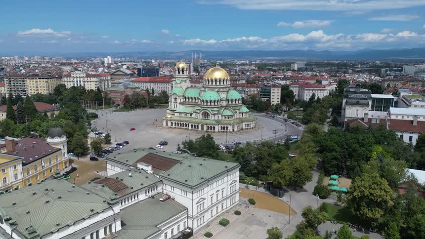 An aerial view captures the alexander nevsky cathedral in tallinn estonia with its golden domes and green roofs amidst a city filled with buildings and trees under a partly cloudy sky