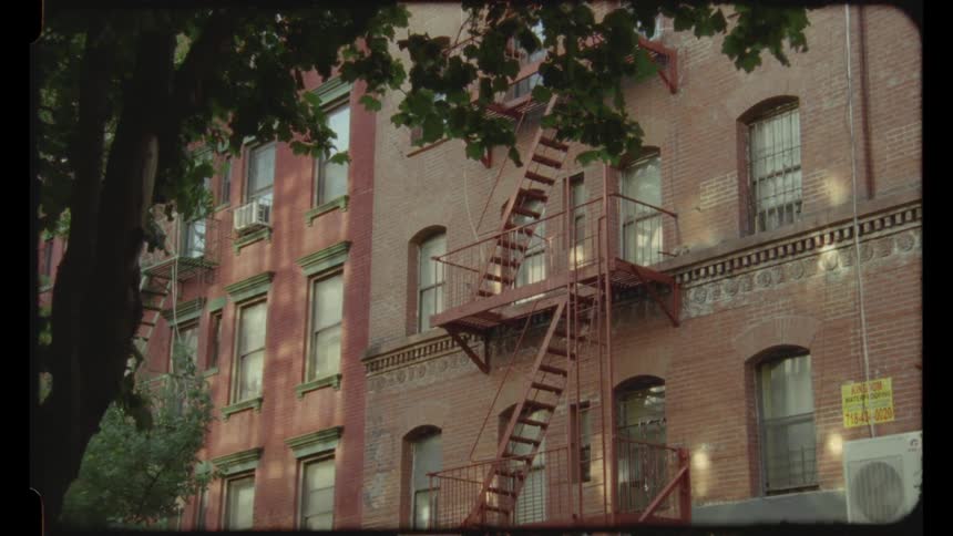 A residential condo building with steel stairs in the backyard and an ac outdoor unit positioned on the ground floor