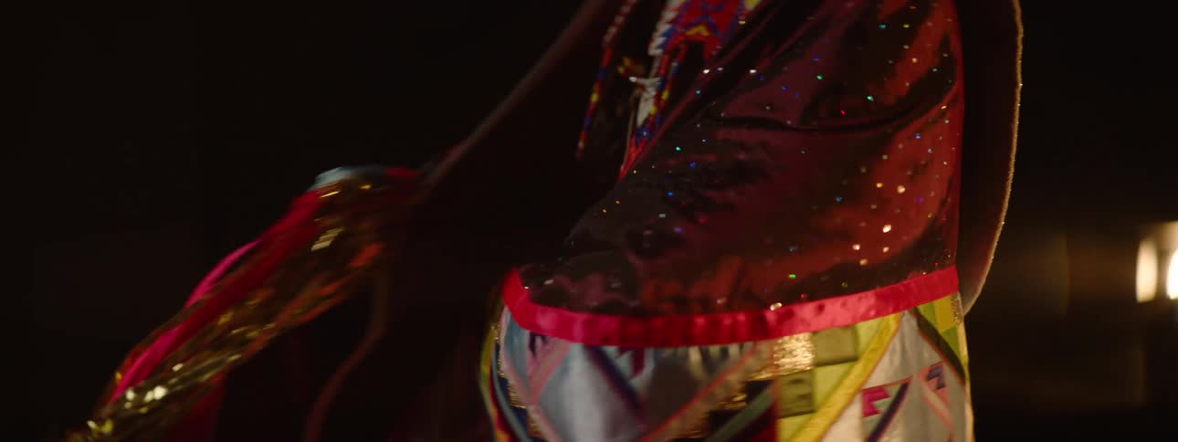 An american indian woman wearing traditional attire stands on a stage proudly showcasing her outfit