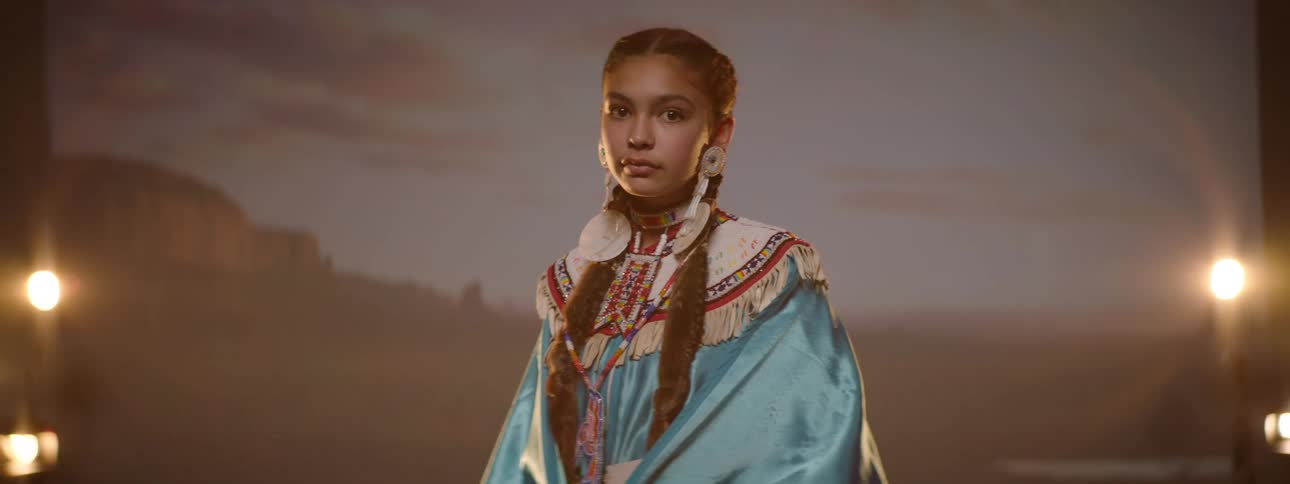 A woman in traditional native garments turns to face the camera