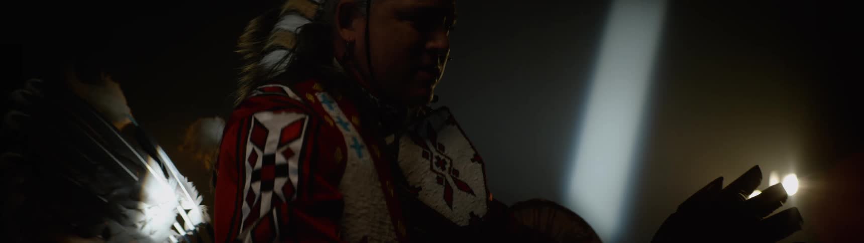 A man indoors wearing red and white clothes is raising his hand forward and sunlight passes in front of his face