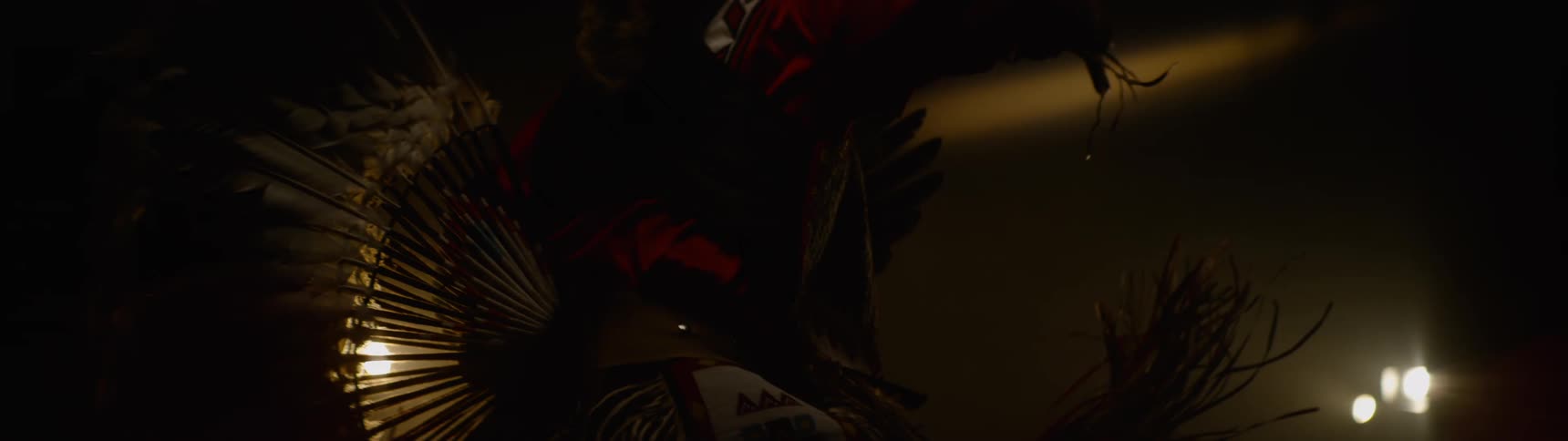 Person wearing traditional native attire dances in a dimly lit area