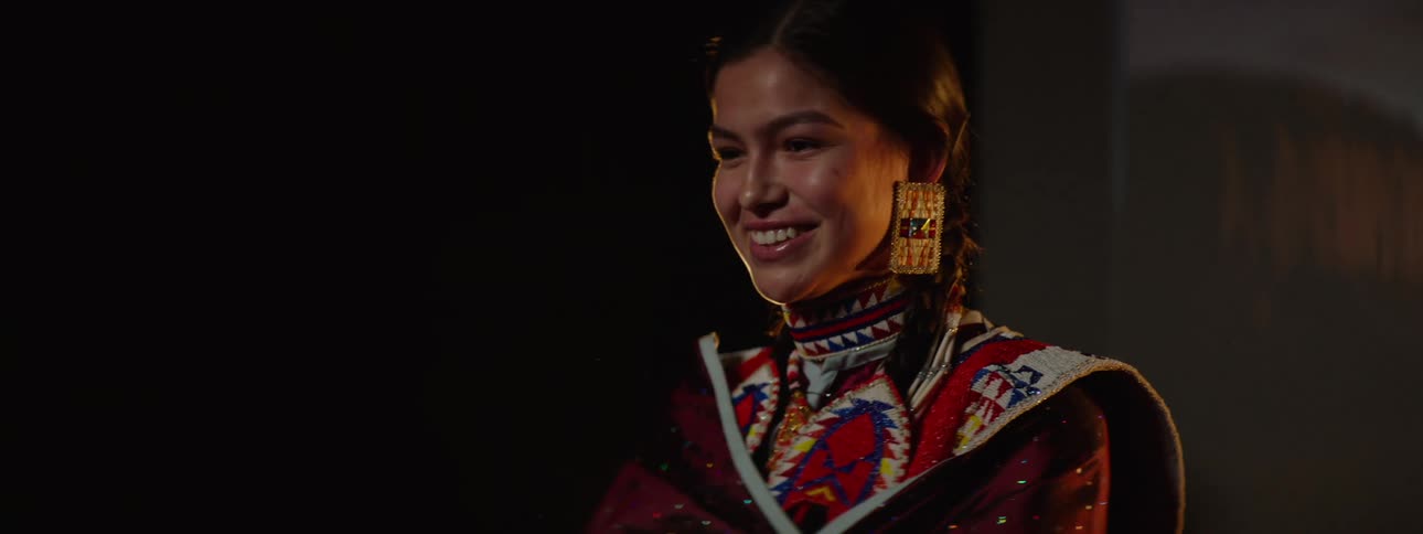 Young woman wearing festive native american attire poses in front of a photography backdrop