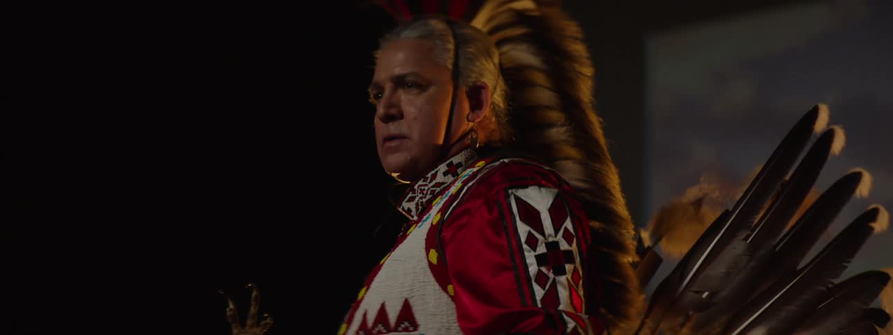 An american indian wearing traditional native attire stands on a stage proudly representing their cultural heritage