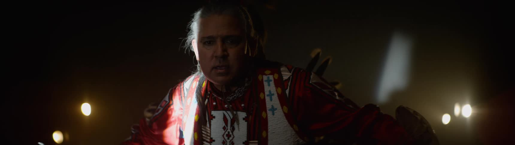 An american indian sits on a stage wearing traditional native attire