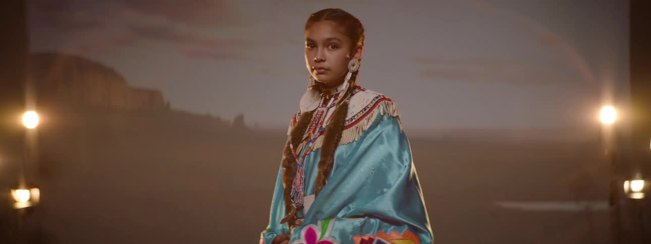 Young woman wearing ceremonial native american attire poses in front of a photography backdrop
