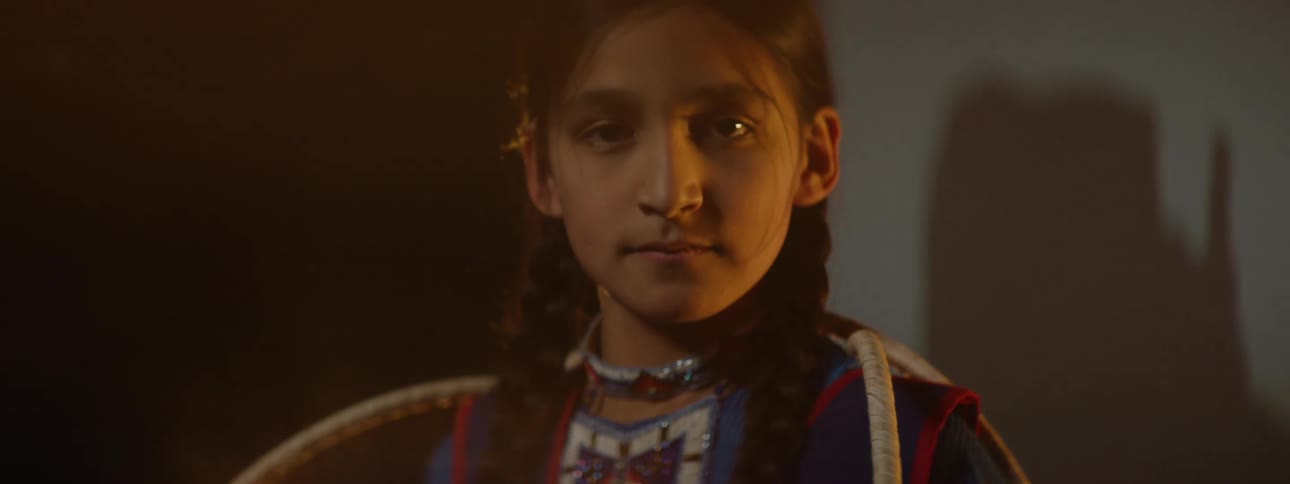A girl wearing beaded tribal clothing stands and looks straight ahead