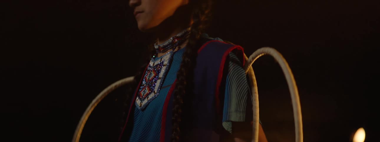 A native american teenage girl smiles and poses in traditional attire holding a series of large circular rings
