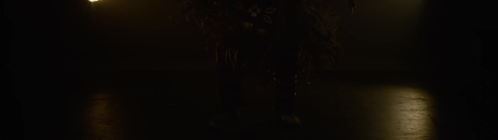 Dancer wearing native american attire dances in a dimly lit area