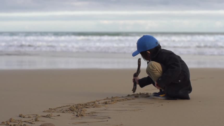Child drawing in the sand at the beach