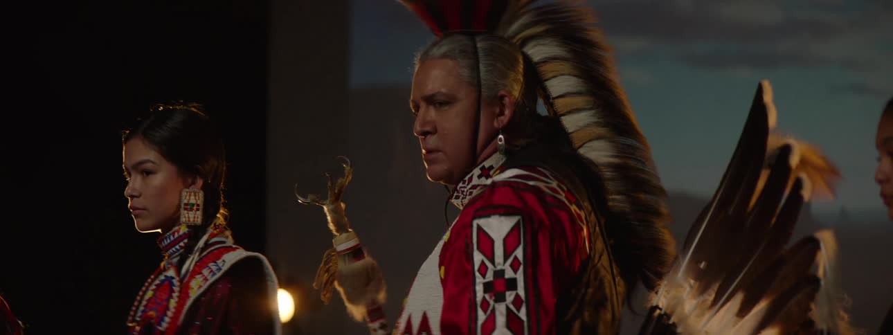 A group of native american indians including a man and several teenage girls all dressed in traditional attire standing on a stage