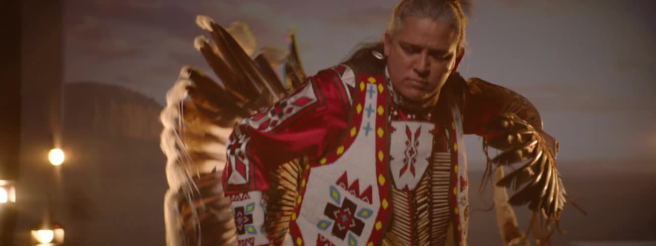 A native american man wearing traditional attire dances on a stage