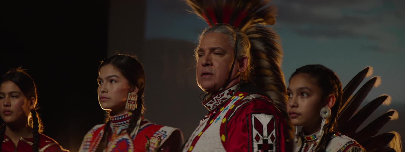Native american group stands solemnly in traditional regalia under warm light