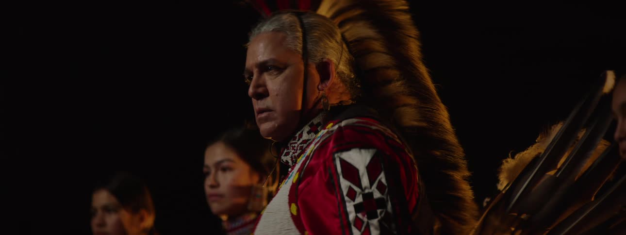 People wearing traditional indigenous clothing in a dimly lit indoor hall