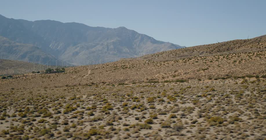 A dry desert landscape with sparse vegetation stretches toward a distant mountain range