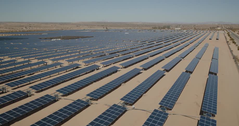 A massive solar farm stretches across a dry desert landscape under clear skies