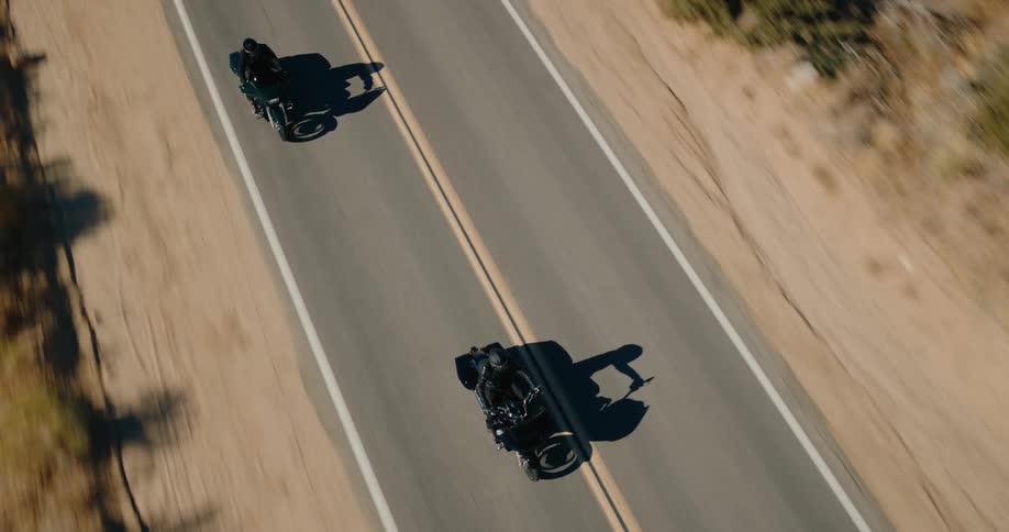 Two individuals each riding a motorcycle on a freeway that runs through a valley on a sunny day