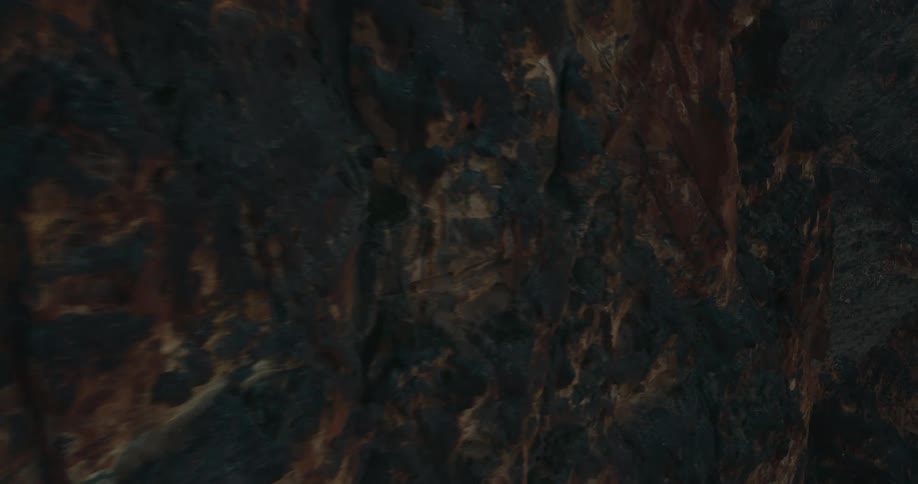 Aerial flyover on the shadowed side of jagged desert red rock mountain peak