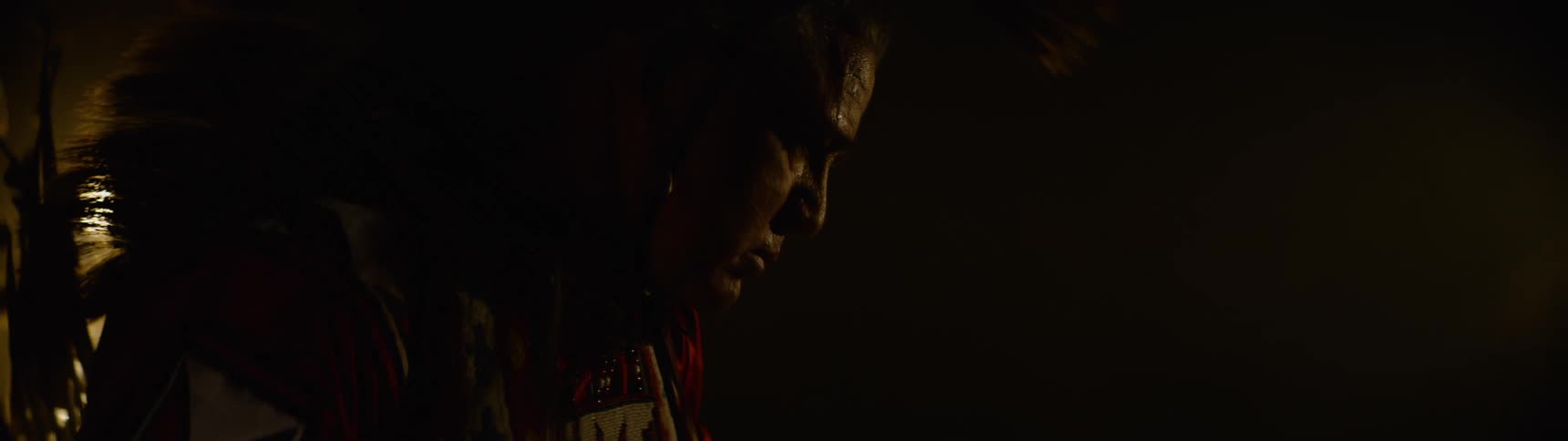 A man wearing a headdress is standing in the dark