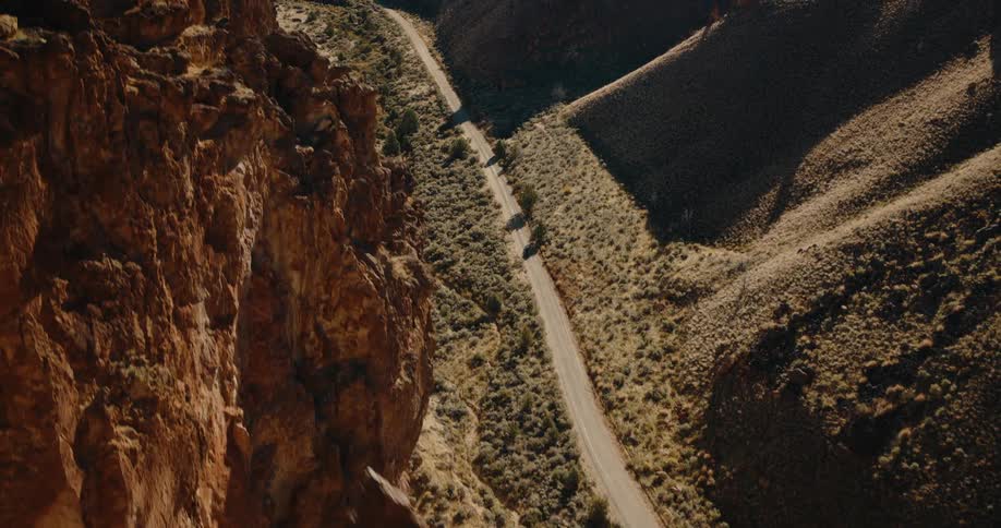 A person riding a motorcycle along a road winding through a valley under the bright midday sun