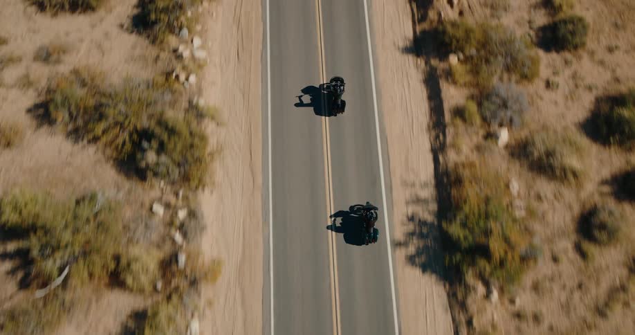 Two motorcyclists ride on a desert highway from a topdown aerial view