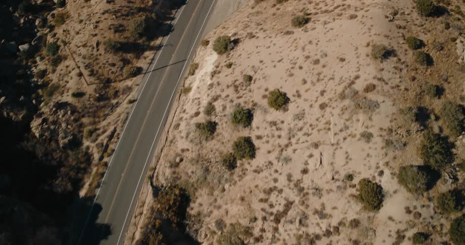 A winding road cuts through a dry rocky desert landscape with sparse vegetation