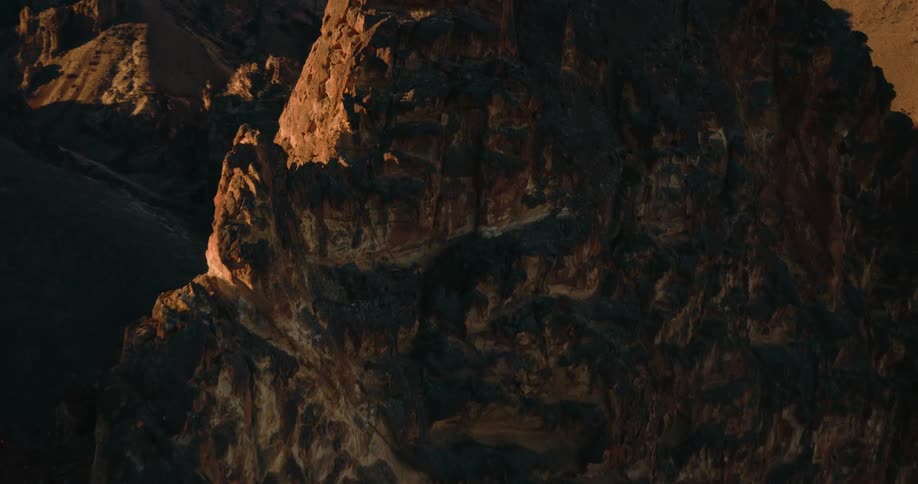 The setting sun flares brightly from behind a rugged shadowy mountain peak casting dramatic light and shadows that sweep across the rock face