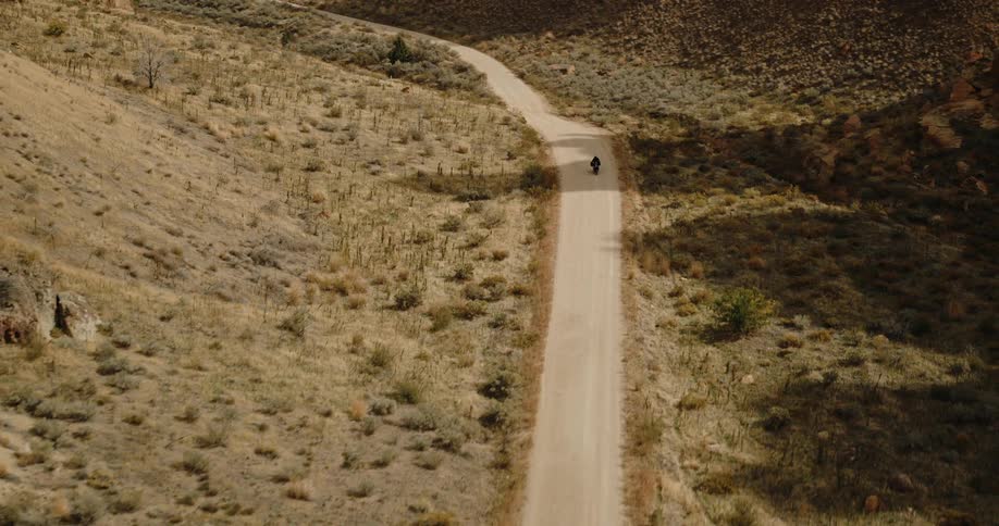 A person rides a motorcycle along a valley road under the bright midday sun