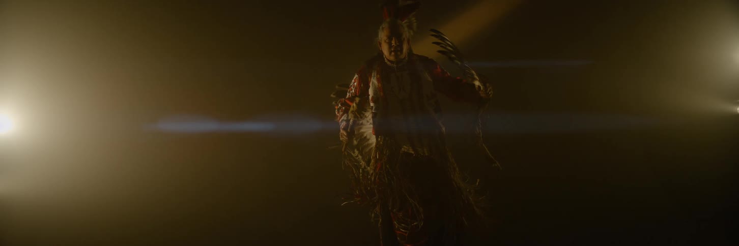 A man is dancing and swinging the feathers on his costume