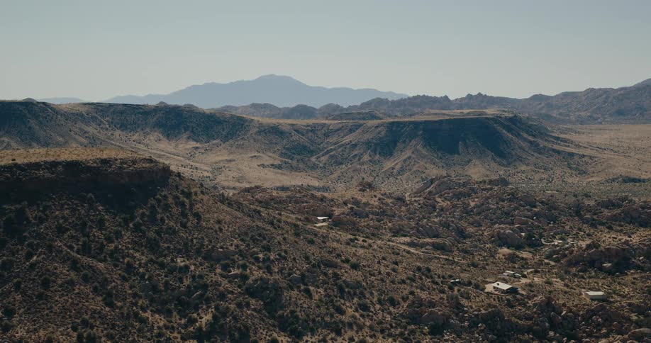 A valley with rolling hills and mountains in the background under a clear midday sky