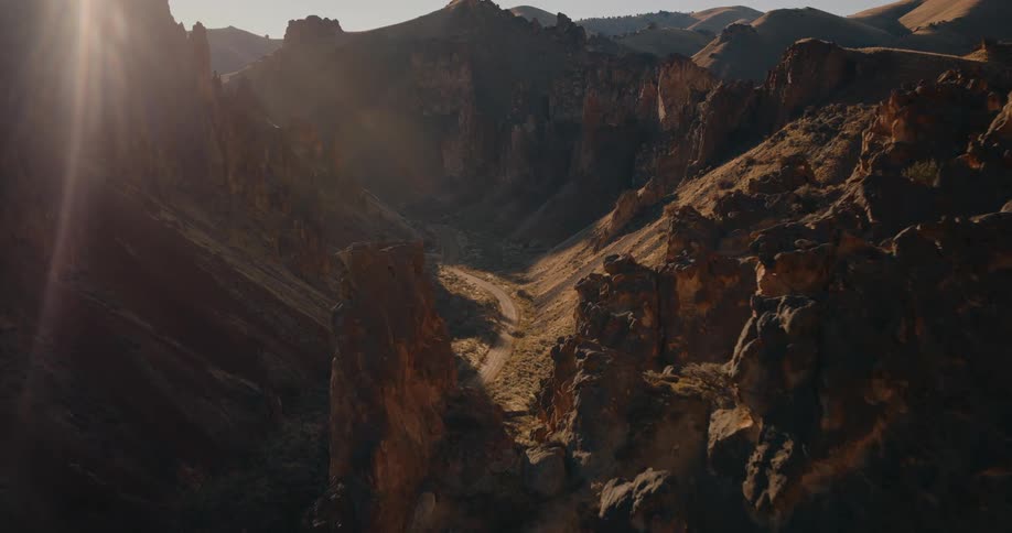A dramatic aerial shot captures a rocky canyon lit by golden sunlight during sunset