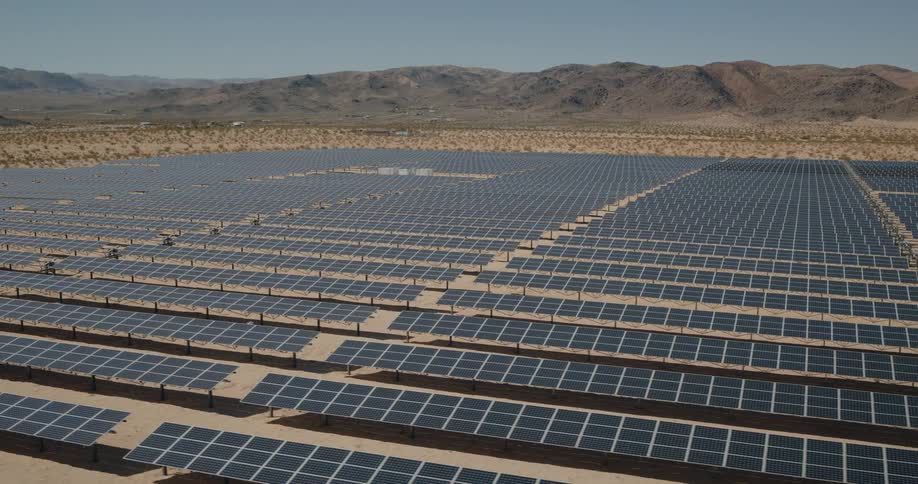 A wide solar farm stretches across a desert landscape under a clear sky