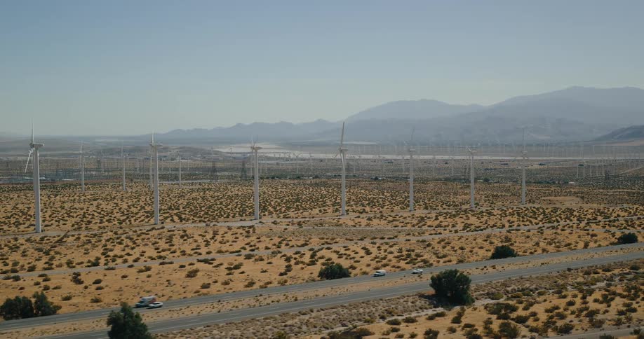 Traffic moves on the road as turbines spin on a wind farm in the desert