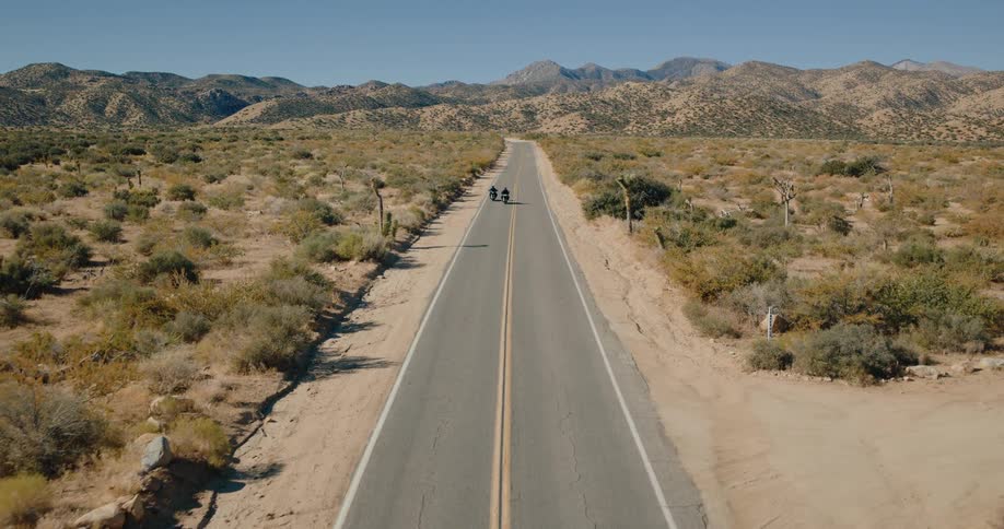 Two people ride motorcycles crosscountry on a freeway on a sunny day